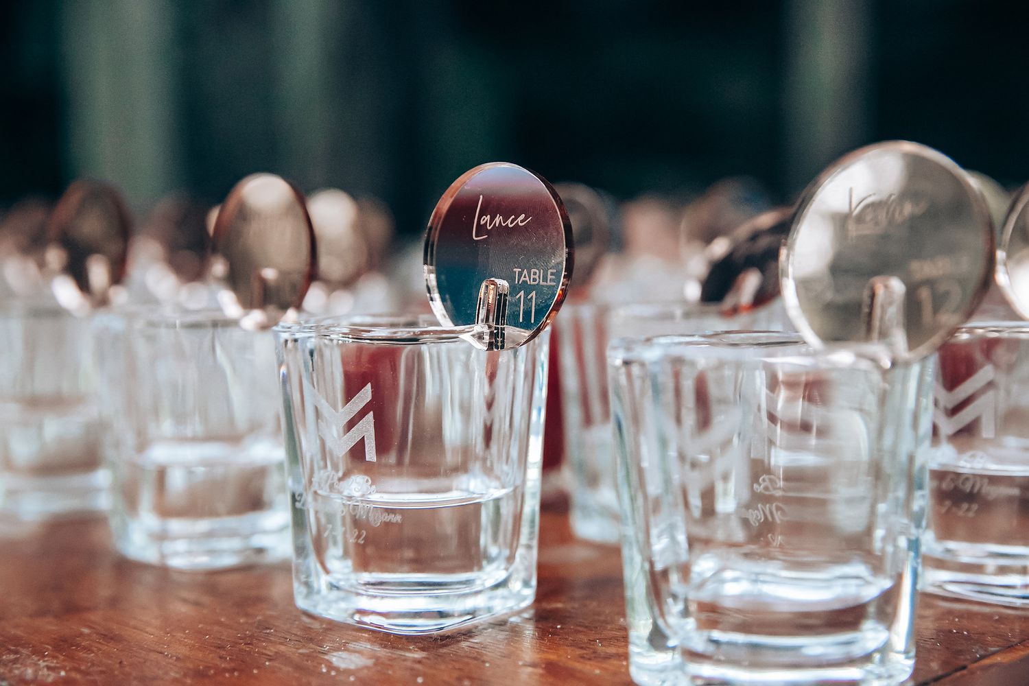 Crystal glasses lined up on a wooden table reflect light and create an elegant dining setting.
