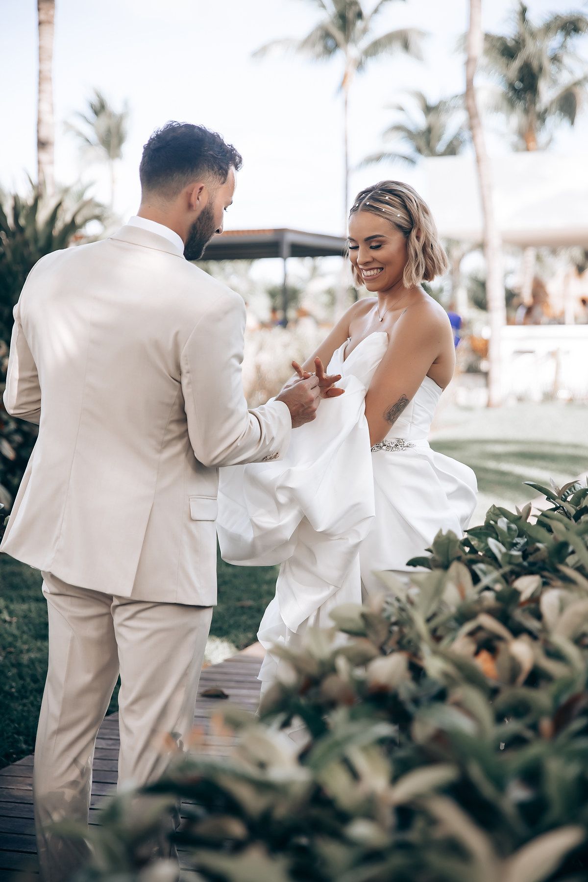 Couple in light colored wedding attire sharing intimate moment on tropical garden path.