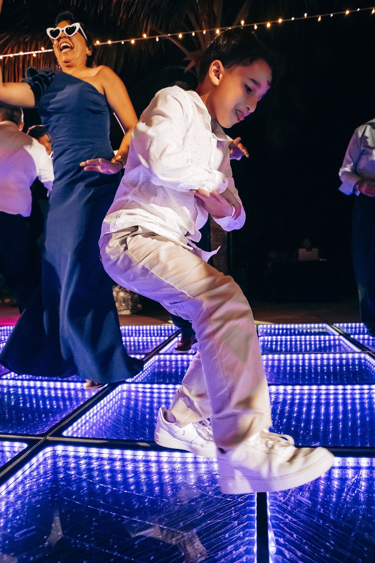 Wedding guests dancing energetically on a glowing blue LED dance floor at night.