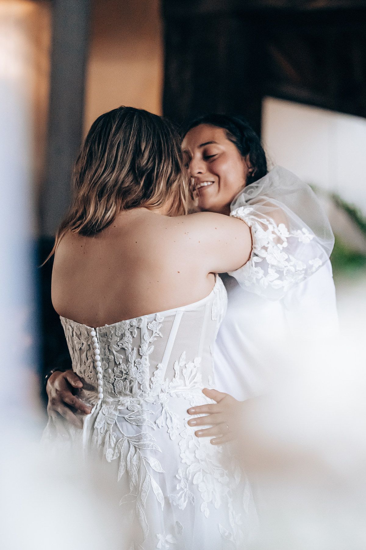 Two people share an intimate embrace at a wedding, with one wearing an elegant white lace wedding dress.