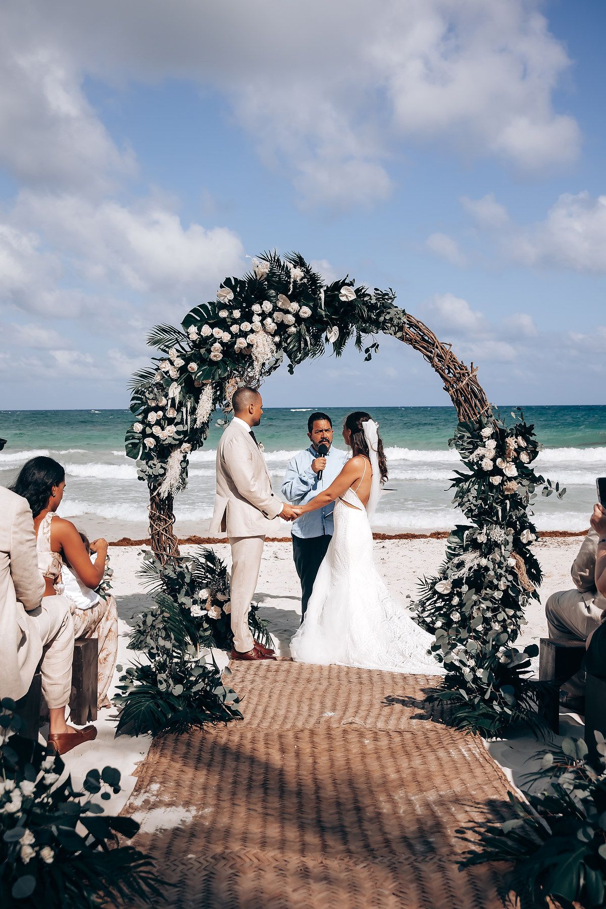 A beach wedding ceremony with a floral arch overlooking turquoise waters and white sand.