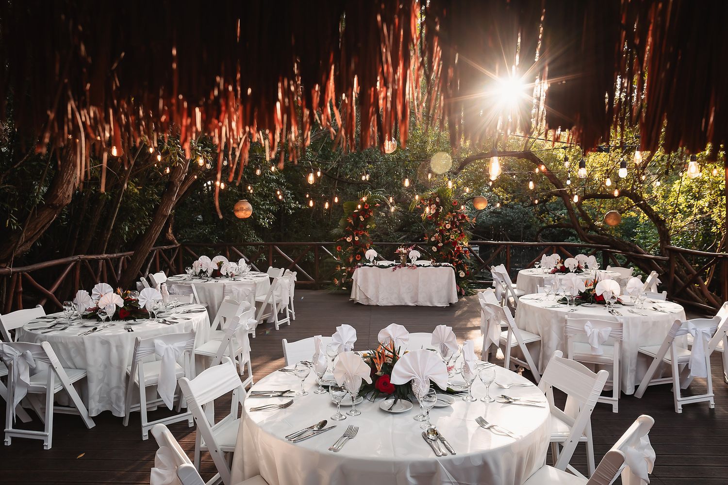 Outdoor wedding reception venue with round tables and white chairs set under twinkling lights at night.