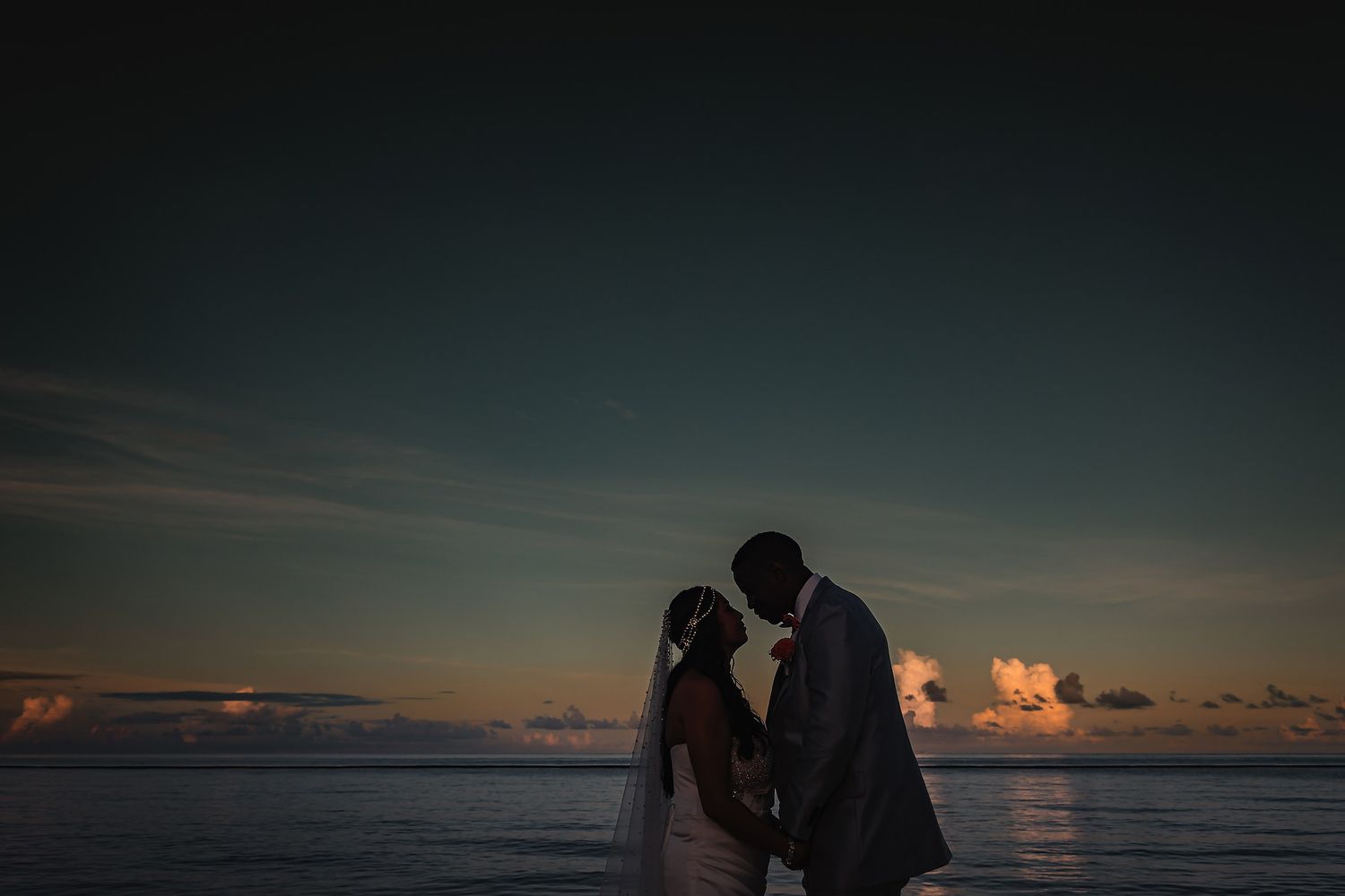 Silhouettes of a wedding party against a dramatic sunset sky over the ocean.