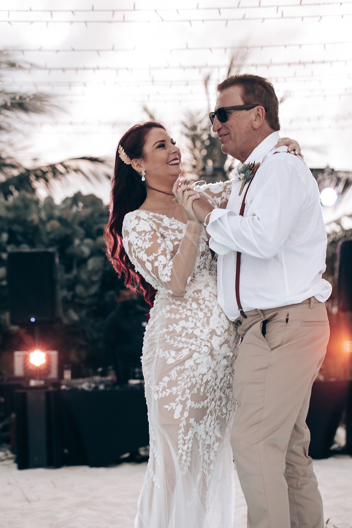 A couple shares a romantic dance at sunset, with the bride wearing a delicate lace gown and groom in tan suit.