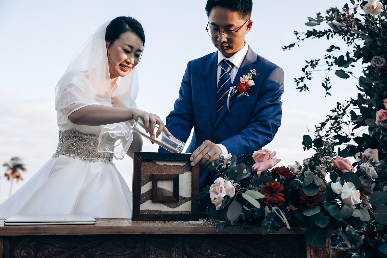 Couple performing traditional unity ceremony with decorative box and floral arrangements.