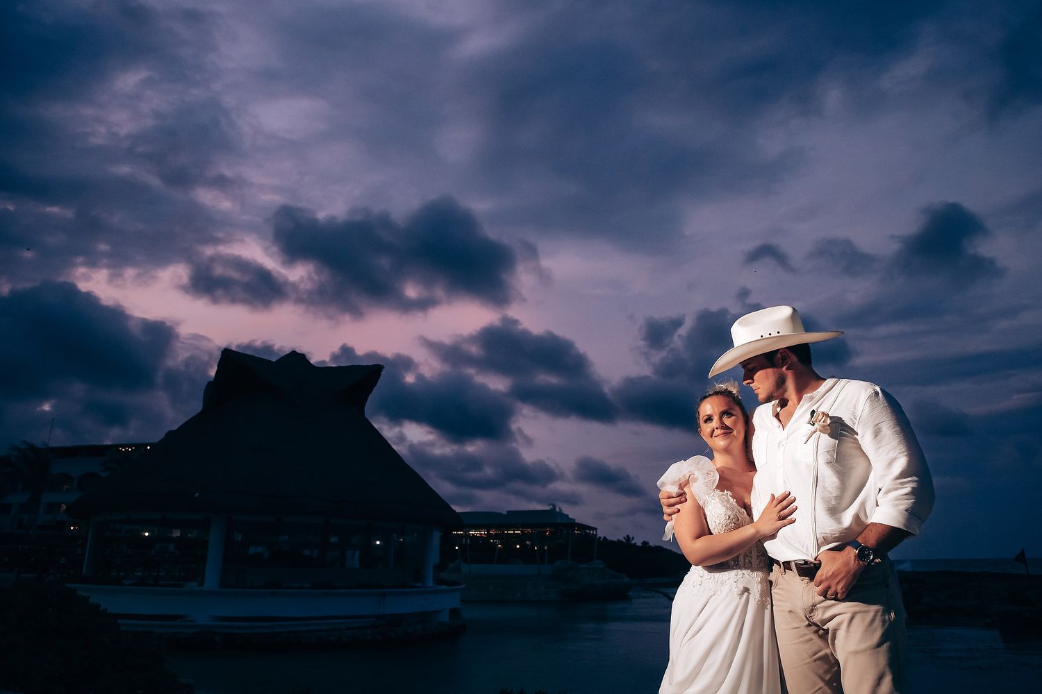 Silhouettes of wedding guests dancing against a dramatic purple sunset sky.