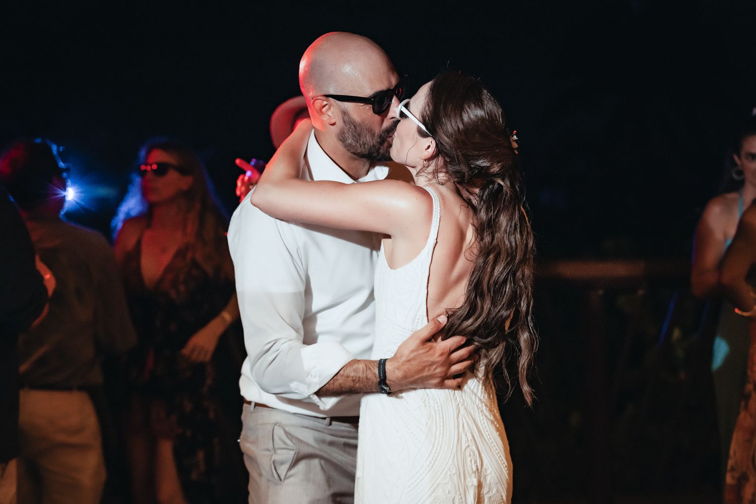 Couple sharing a romantic kiss on the dance floor at an outdoor evening wedding reception.