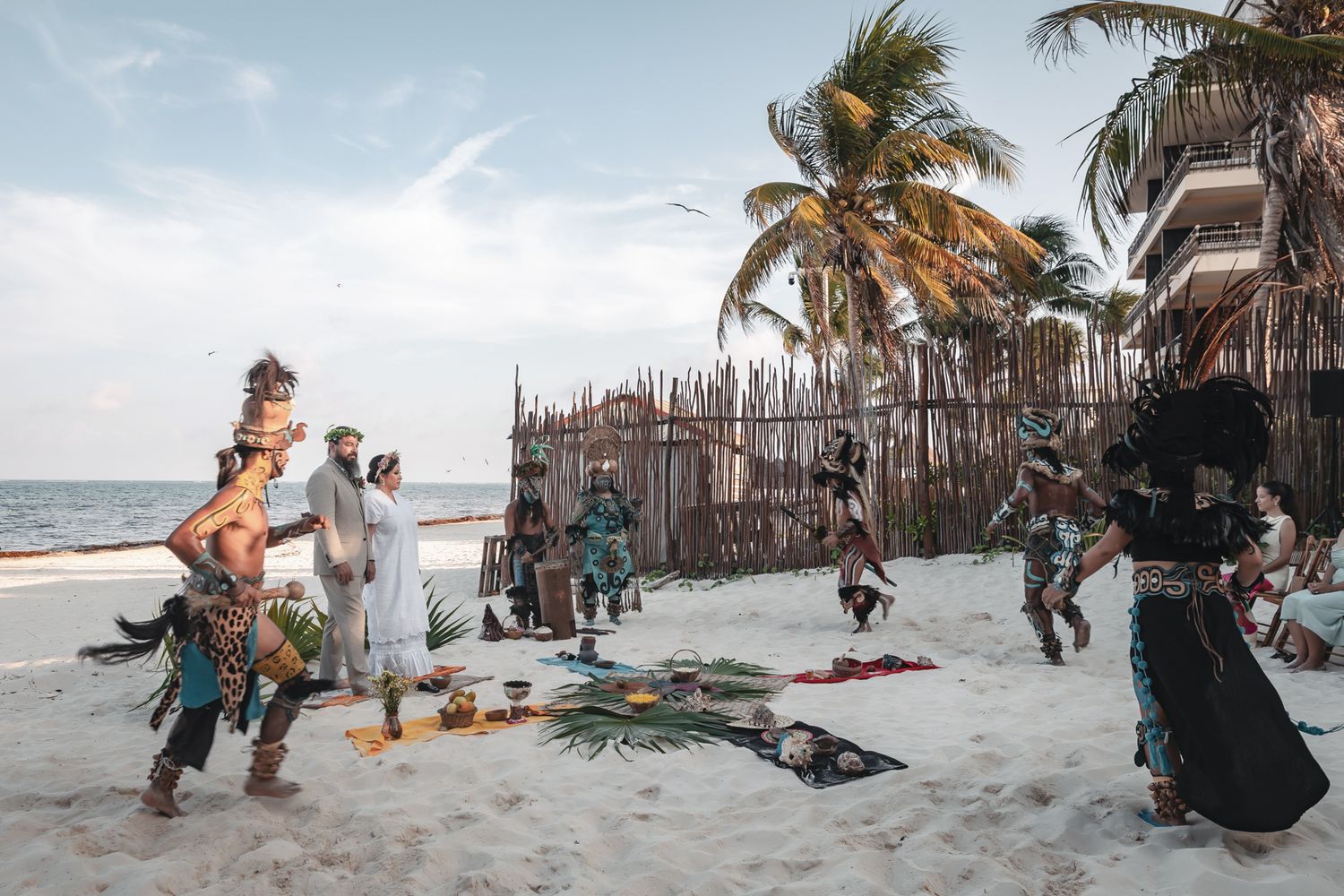 Indigenous performers in traditional Mayan costumes conduct a ceremonial ritual on a tropical beach in Tulum, Mexico.