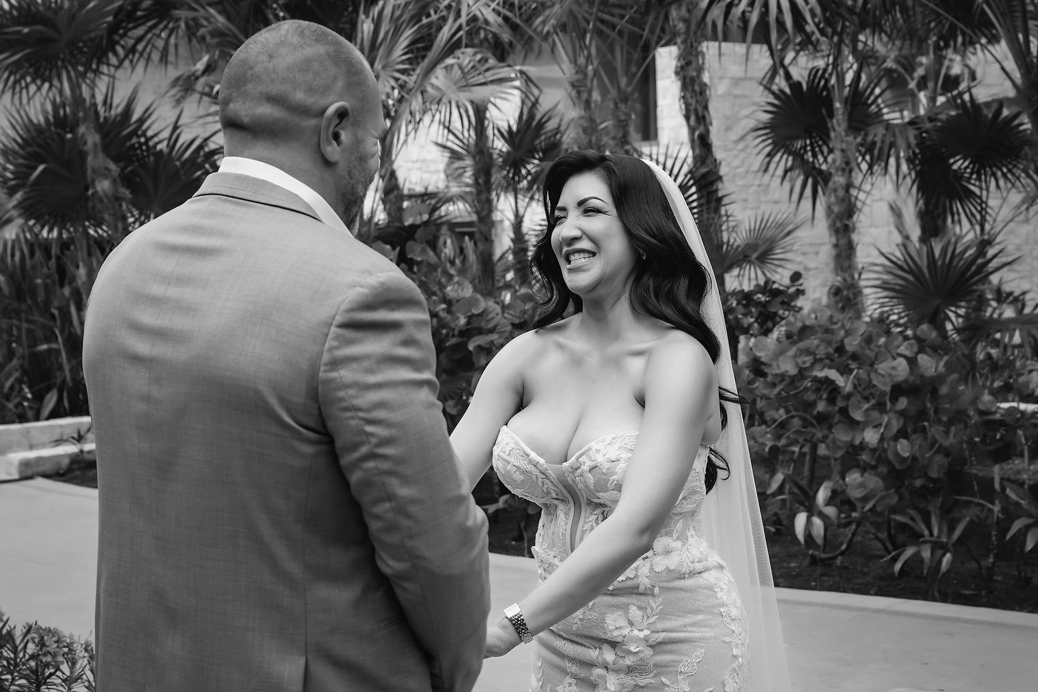 Black and white photo of a smiling bride in a strapless gown holding hands with groom at outdoor wedding ceremony.