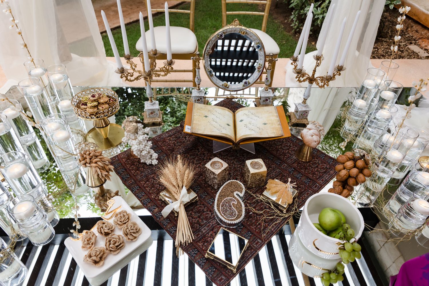 Elegant wedding sofreh aghd display with open book, candles, sweets, and decorative items on striped black and white tablecloth.