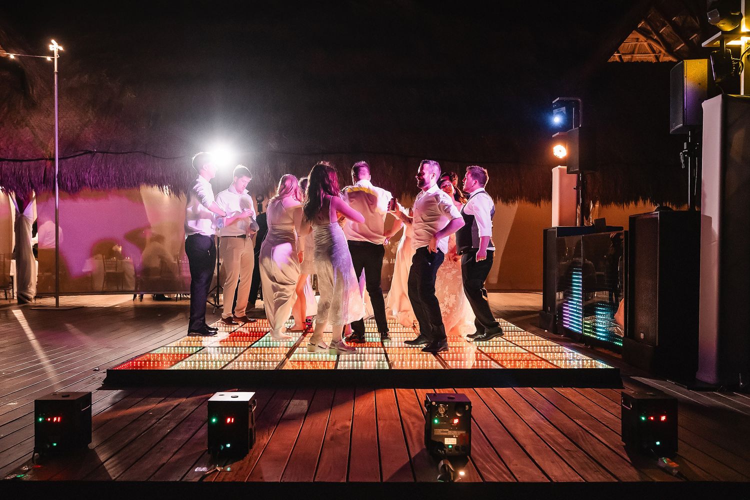 Group of people dancing on illuminated dance floor at outdoor night wedding reception party.