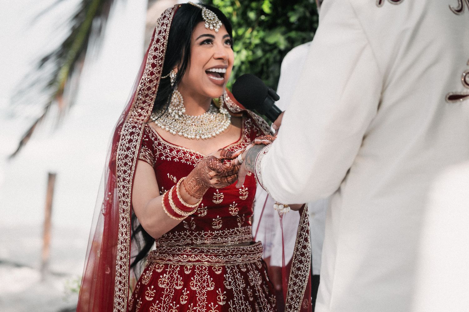 Radiant Indian bride in red lehenga laughing joyfully during traditional wedding ceremony.