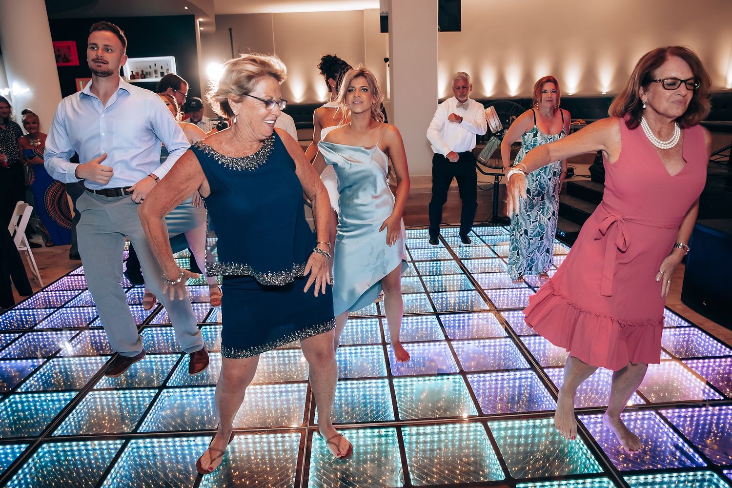 Guests dancing on a colorful LED light-up dance floor at a wedding reception.