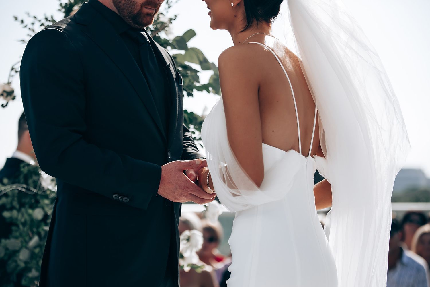 Wedding ceremony moment captured with flowing white dress and formal attire against light background.