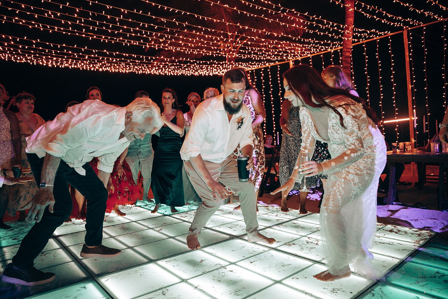 Wedding guests dancing on illuminated LED dance floor under string lights.