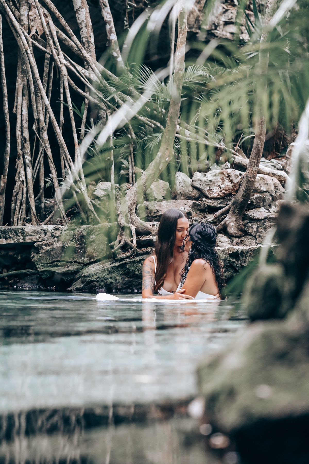 Two people enjoy a romantic moment in a natural swimming hole surrounded by mangrove trees.