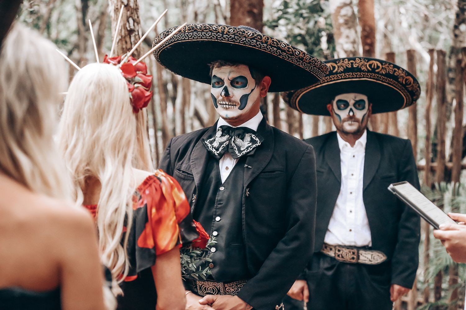 Wedding guests in Day of the Dead makeup and traditional Mexican sombreros at forest ceremony.