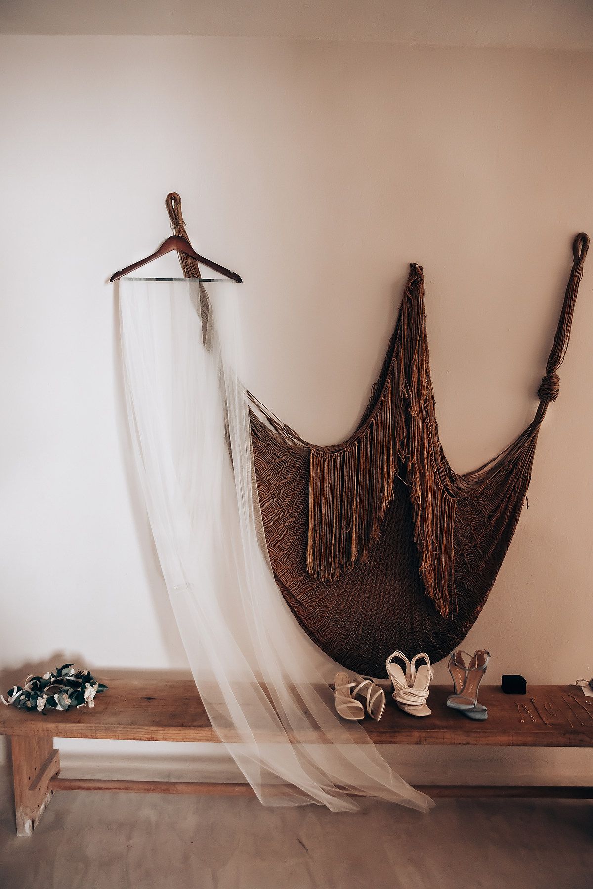 A wedding dress veil hangs on a wooden hanger next to brown dresses and shoes on a rustic shelf.