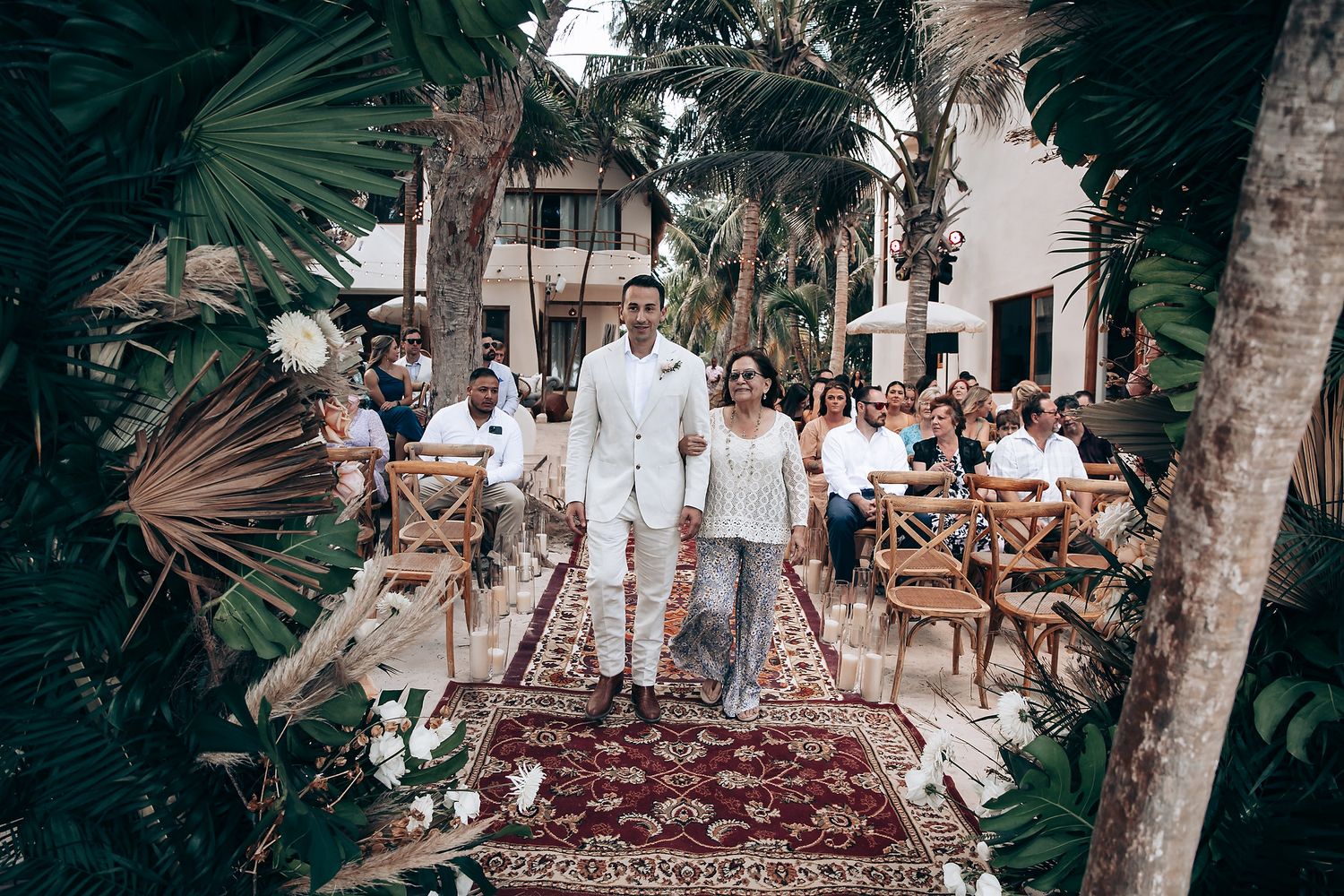 A wedding ceremony setup with white decor and Persian rug aisle runner surrounded by tropical palms.