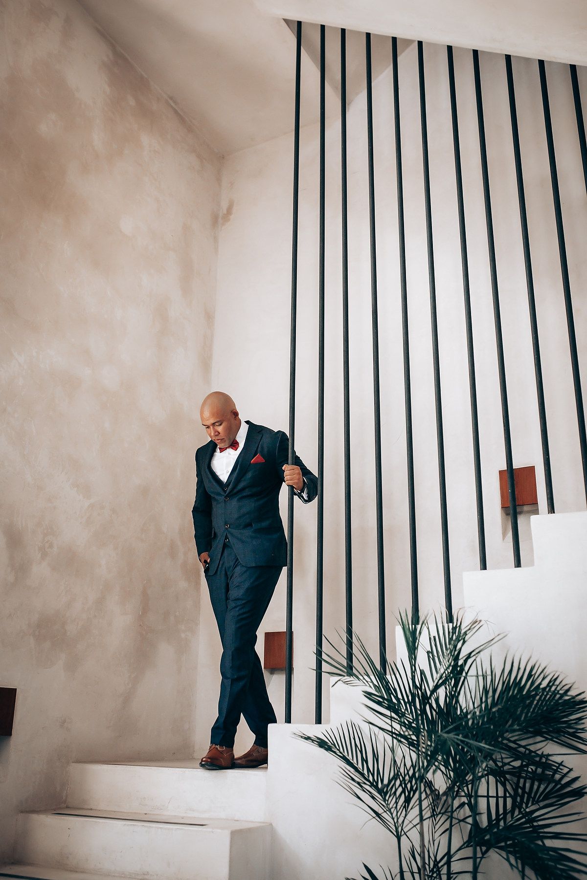A person in a navy suit descends white stairs with modern black vertical railings.