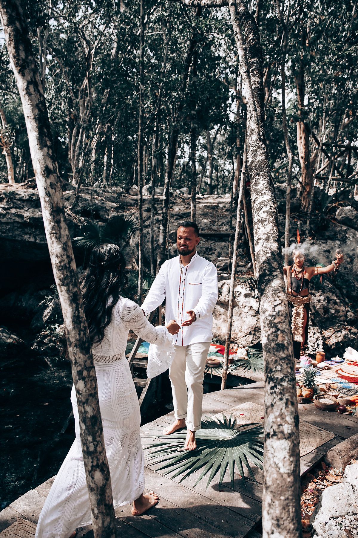 A spiritual ceremony takes place in a wooded area with people dressed in white performing rituals.