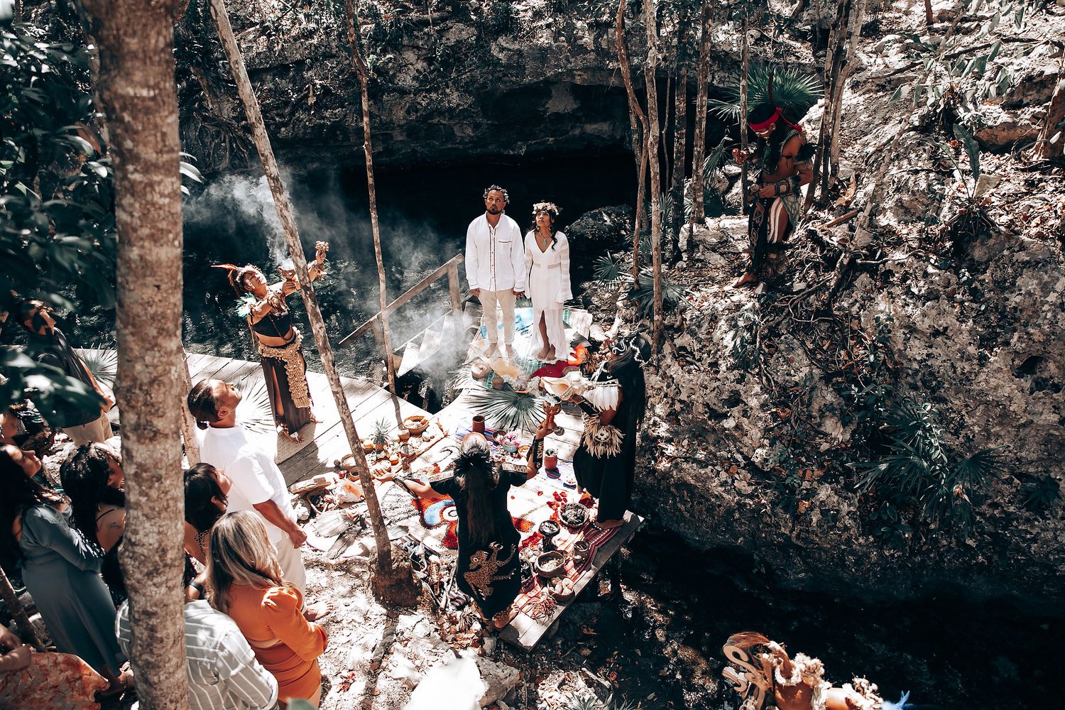 Wedding celebration in a forest clearing with guests gathered around.