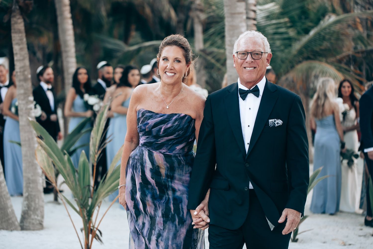 Elegant outdoor wedding ceremony with palm trees and guests seated under a white canopy.