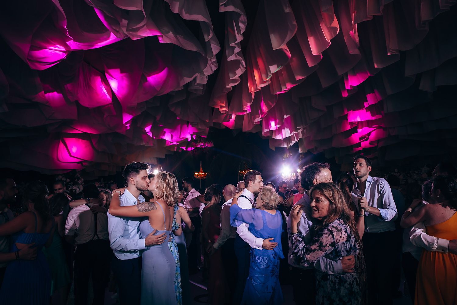Vibrant nightclub-style wedding reception with magenta lighting and dancing guests.