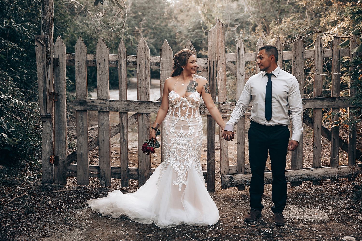 Romantic wedding portraits taken along a rustic wooden fence in a forest setting.