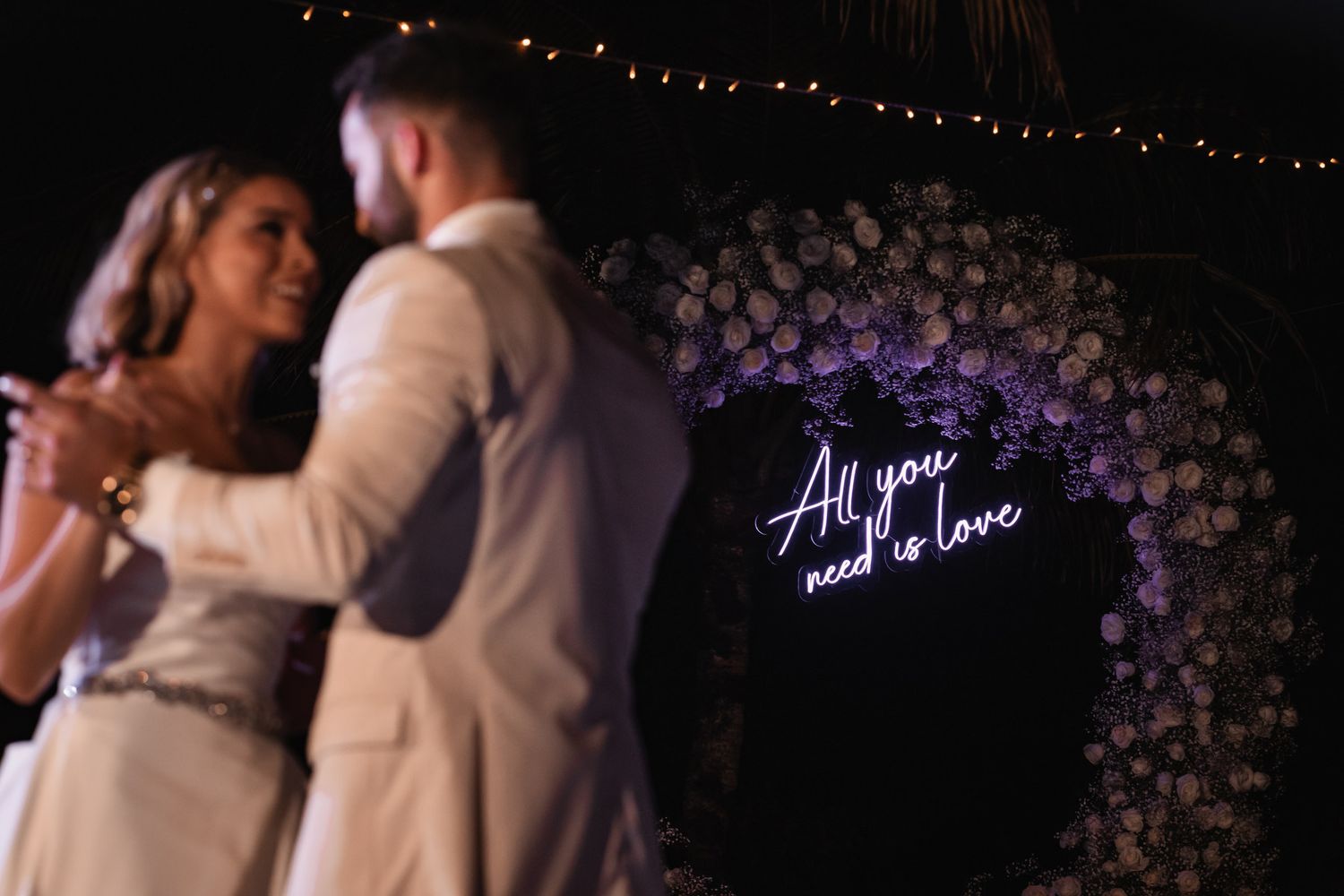 Couple dancing near neon All You Need Is Love floral sign.