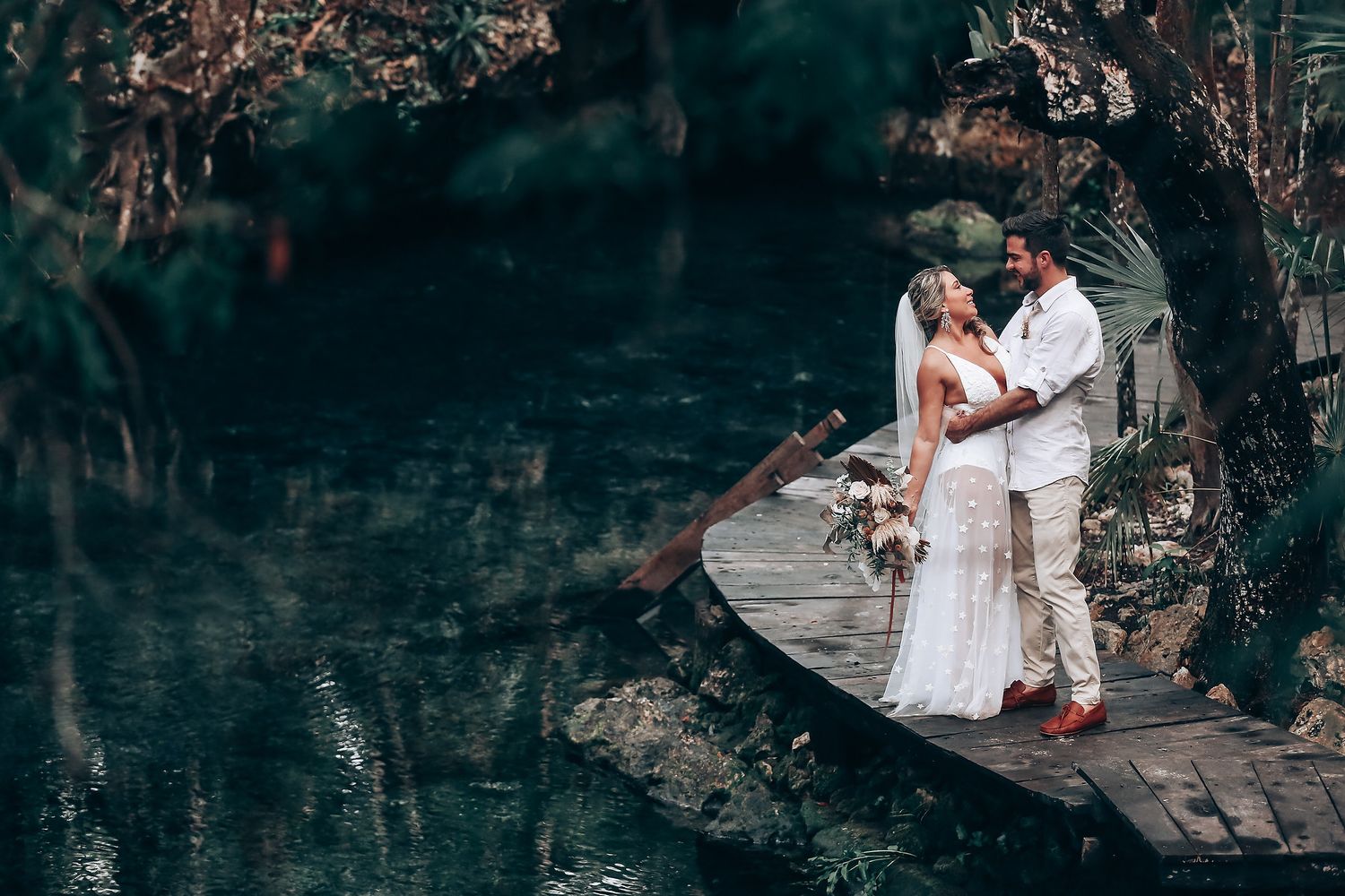 A couple shares an intimate moment on a wooden platform surrounded by forest greenery.