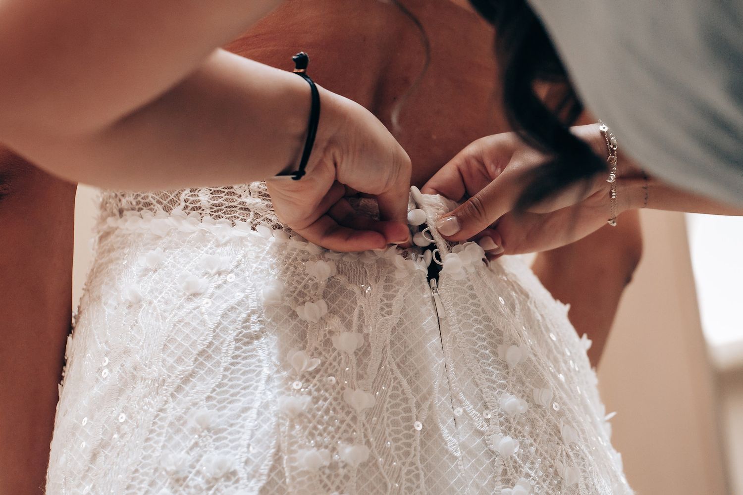 Close-up details of a white lace wedding dress being fastened.
