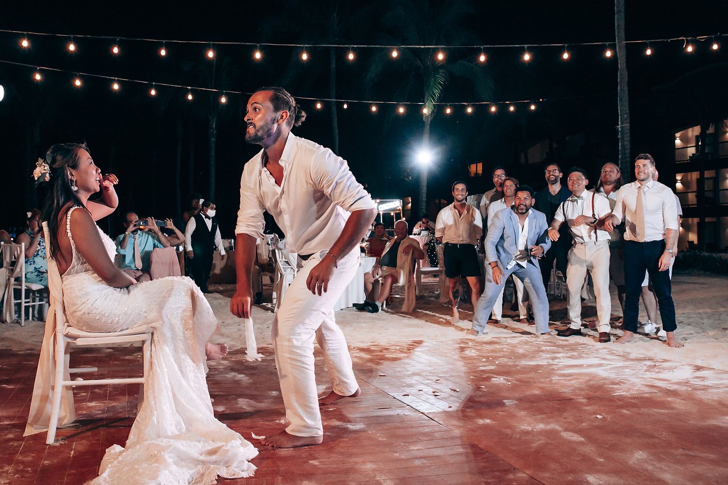 Wedding reception dance floor under string lights with guests dancing in white attire.