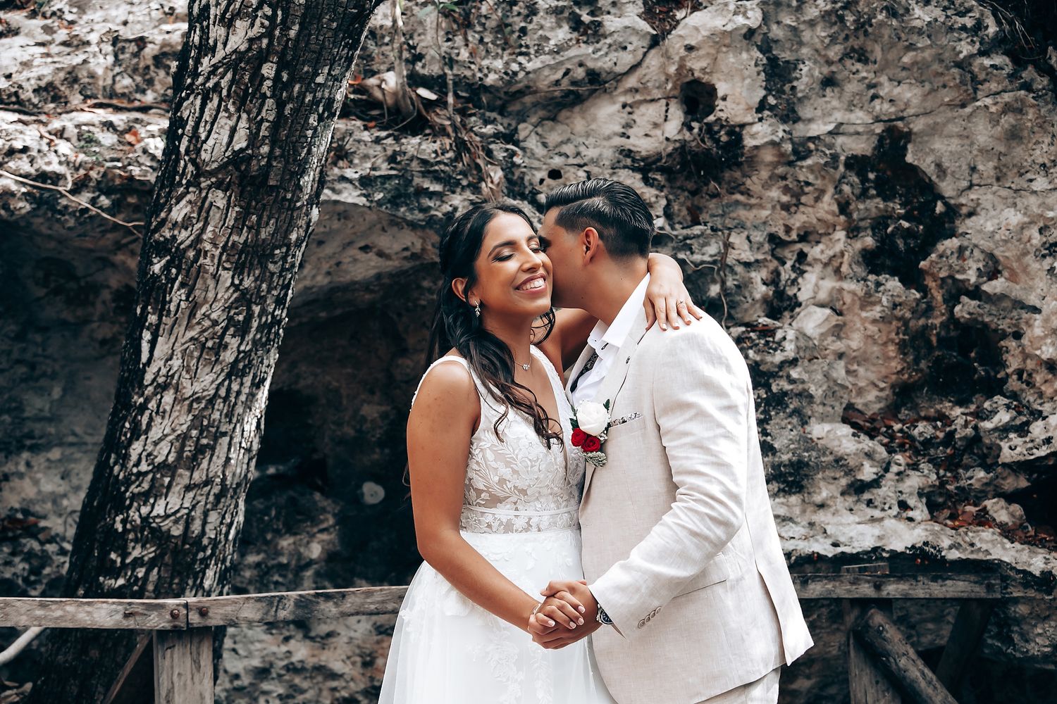 A romantic couple in wedding attire shares tender moments against a rustic stone wall background.
