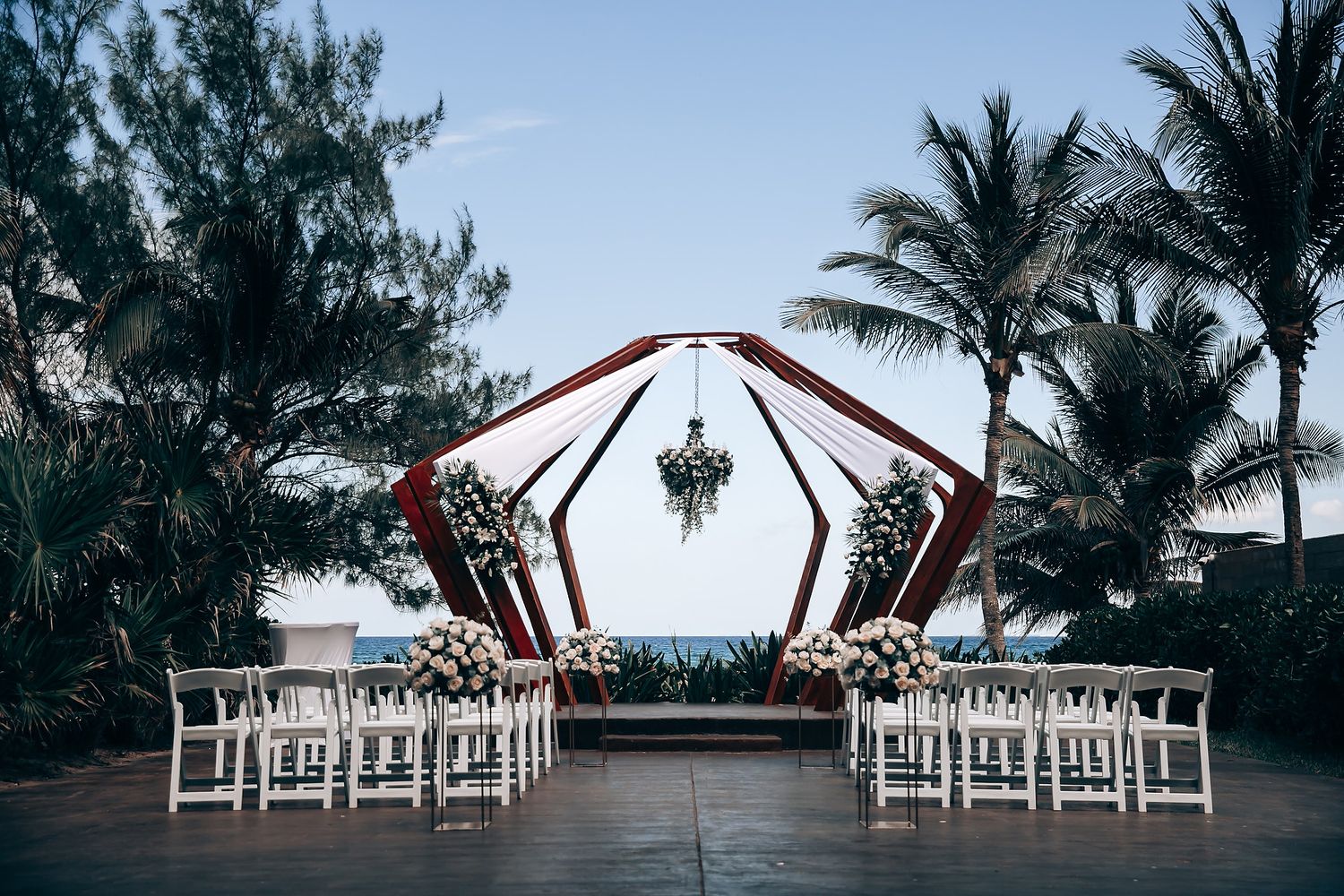 White chairs arranged in rows for an outdoor beach wedding ceremony with palm trees and ocean views.