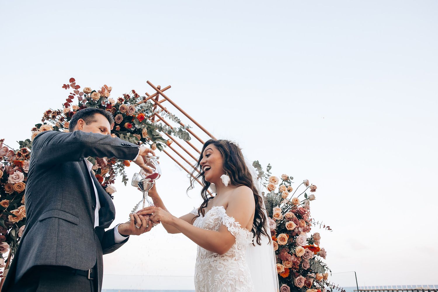 Joyful celebration under a flower-adorned arch by the sea.