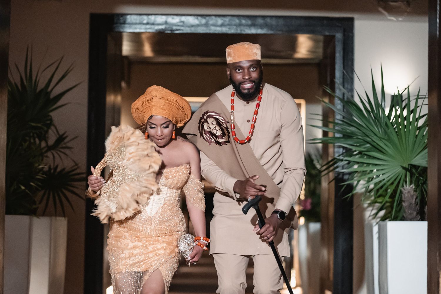 Bride and groom in vibrant Nigerian traditional wedding outfits make a grand entrance together.