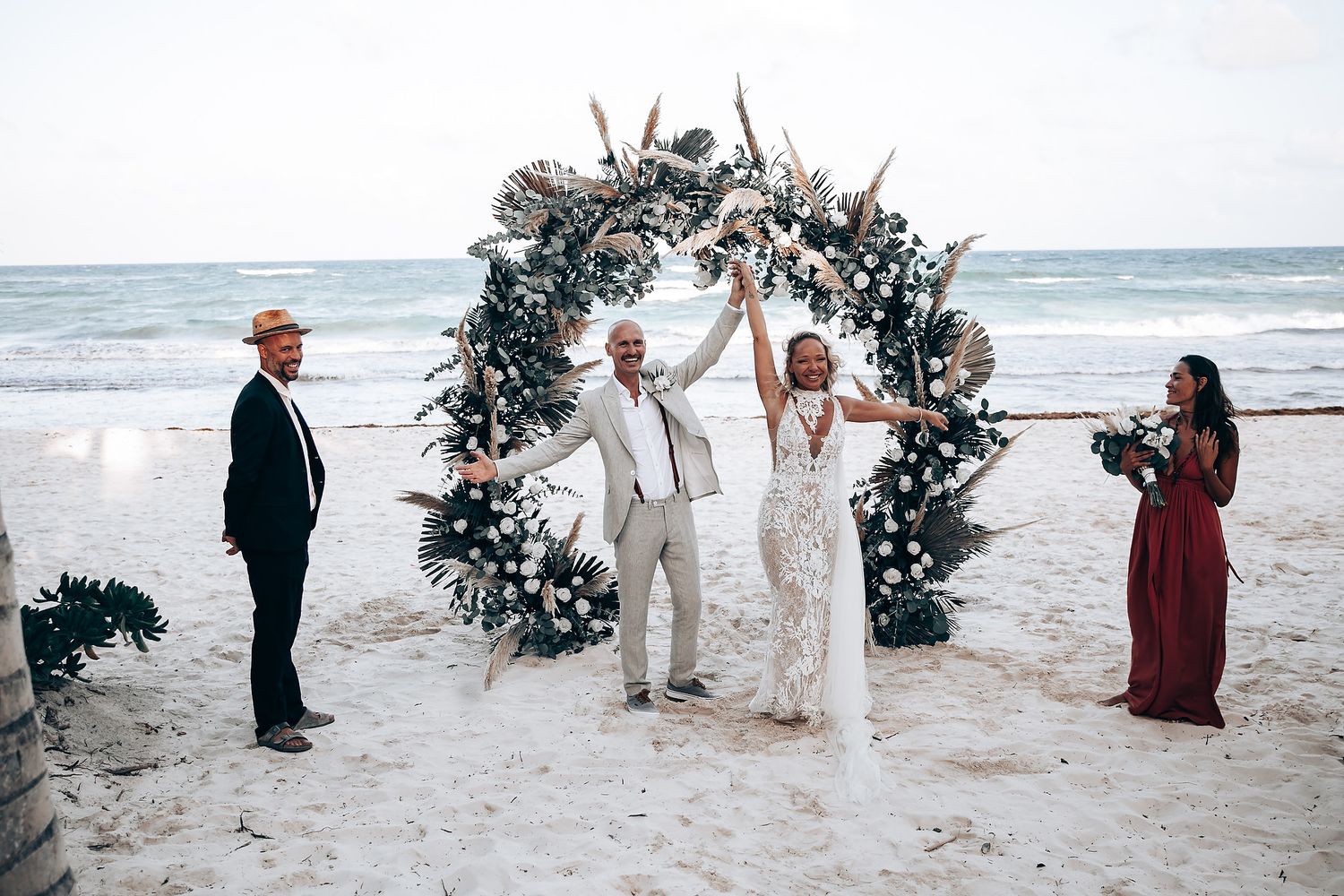 Wedding guests gather on a beach near a floral arch for an intimate ceremony.