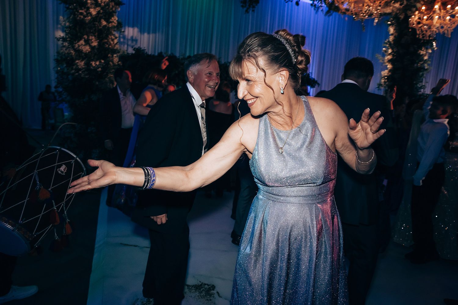 Dancing guest in a silver evening gown enjoying the reception under blue lighting.
