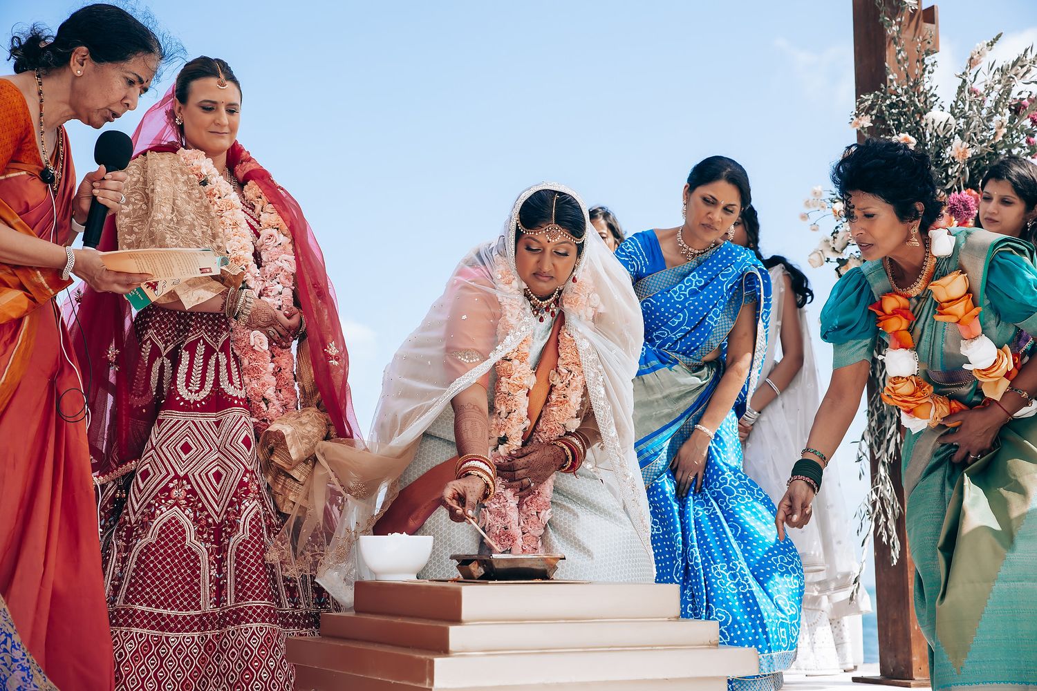 Colorful wedding celebration with guests in traditional attire dancing at a beachside venue.