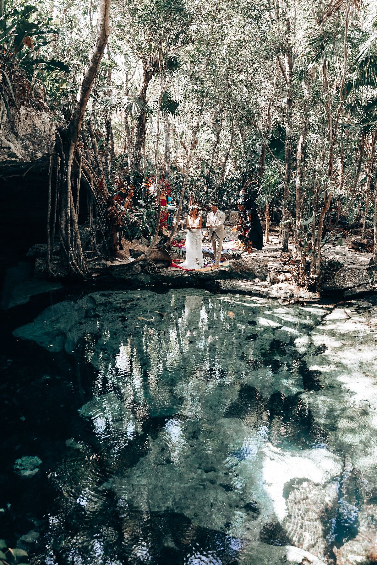 Serene cenote with crystal clear turquoise water surrounded by lush jungle vegetation.