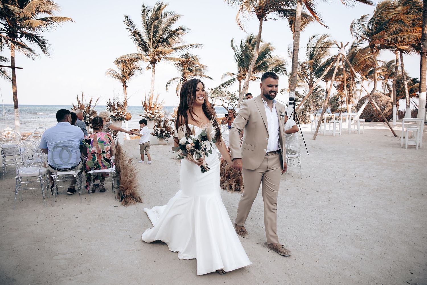 A beach wedding celebration with palm trees swaying in the breeze as guests gather on the sandy shore.