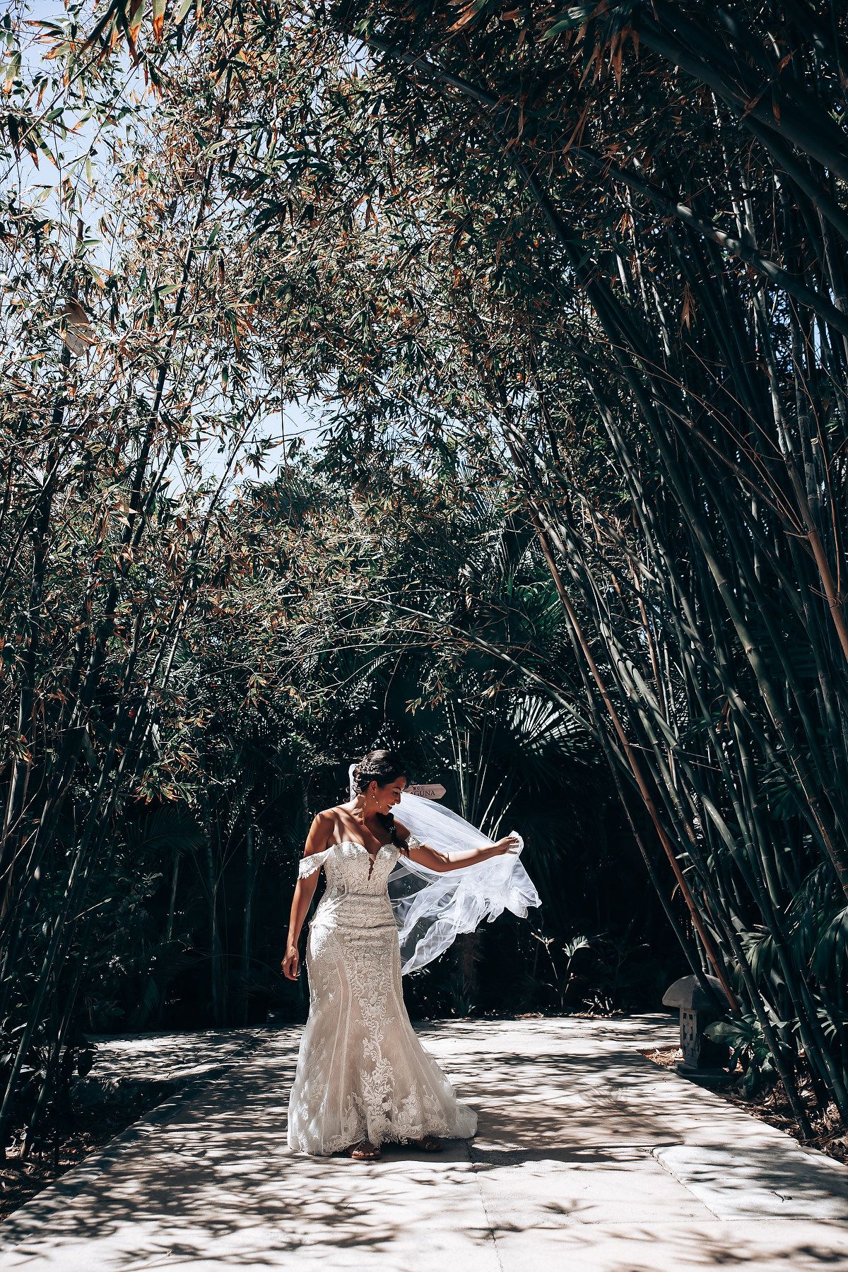 A white wedding dress flows gracefully against a backdrop of tropical bamboo and natural sunlight.