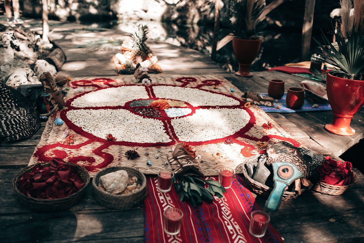 A colorful, intricate mandala design made of flowers, leaves, and other natural materials on a wooden surface.