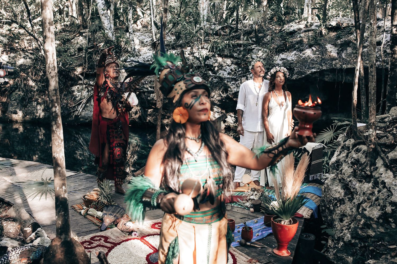 A group of people dressed in traditional tribal attire stand in a forested area.