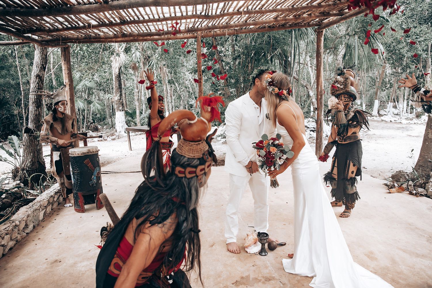 A wedding ceremony incorporating traditional Mayan rituals takes place under a wooden pergola in the forest.