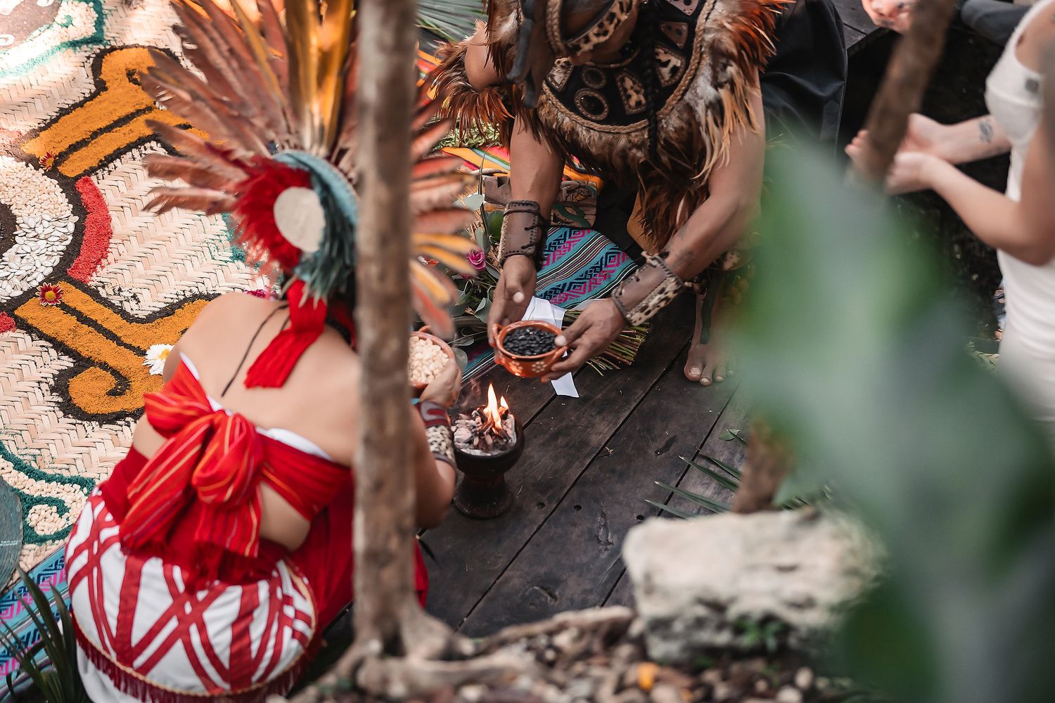 People in traditional indigenous ceremonial attire gather around a ritual fire during a cultural ceremony outdoors.