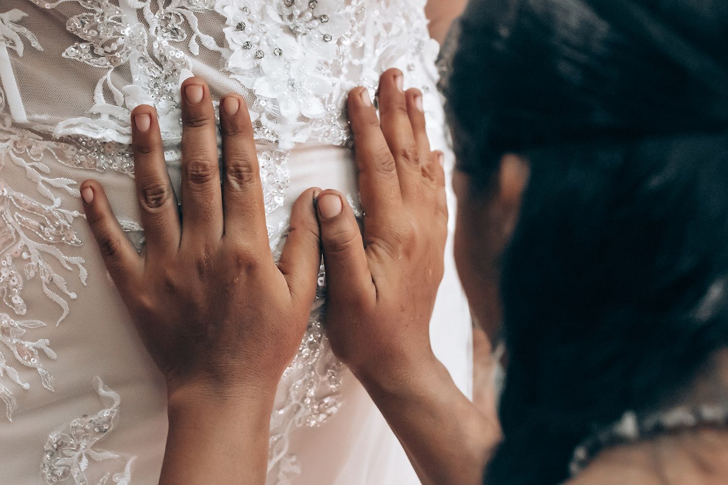 Close-up detail of lace wedding dress with hands touching delicate fabric.