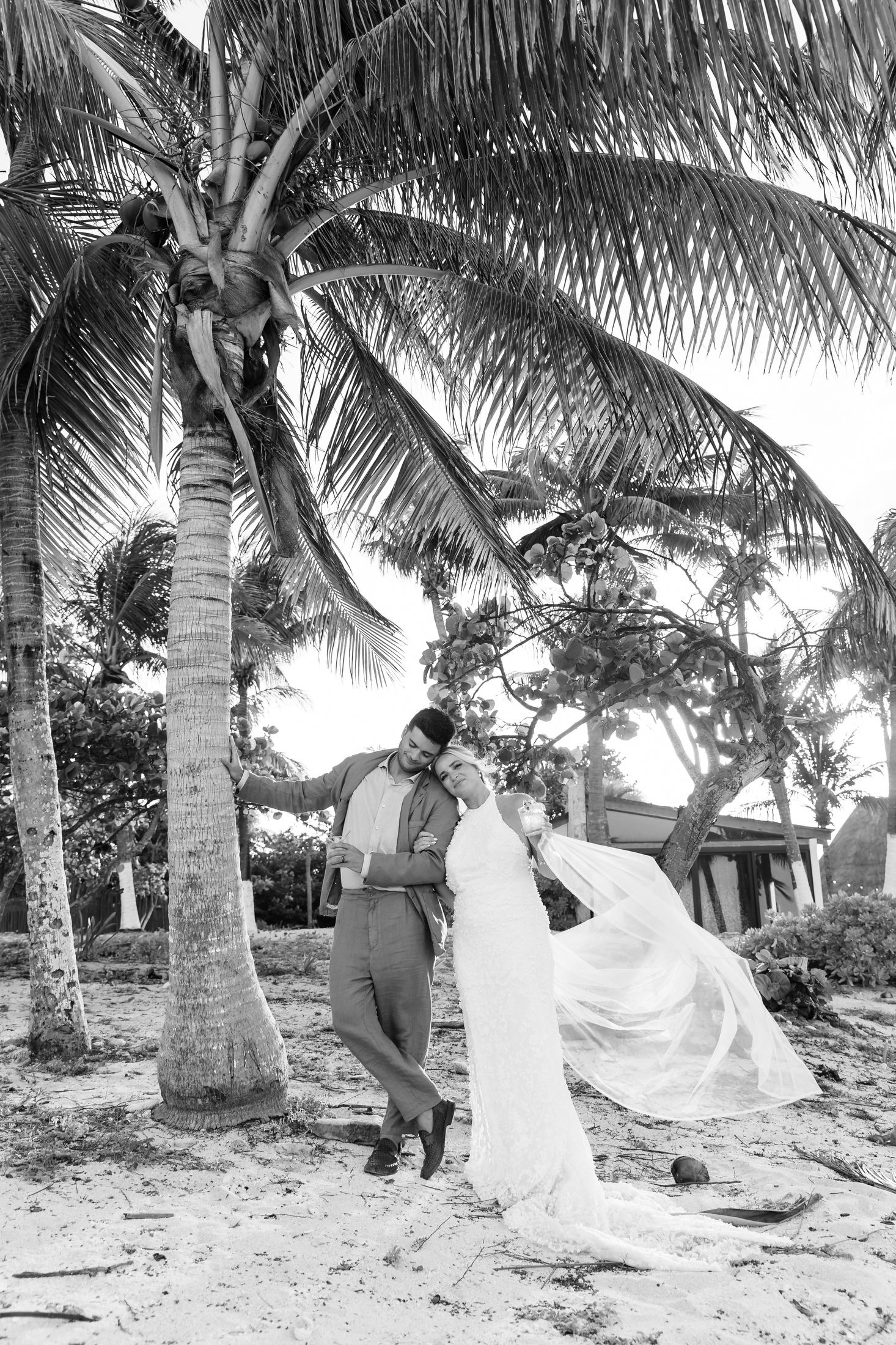 Black and white photo of a couple dancing under palm trees on a sandy beach, bride in flowing white gown.