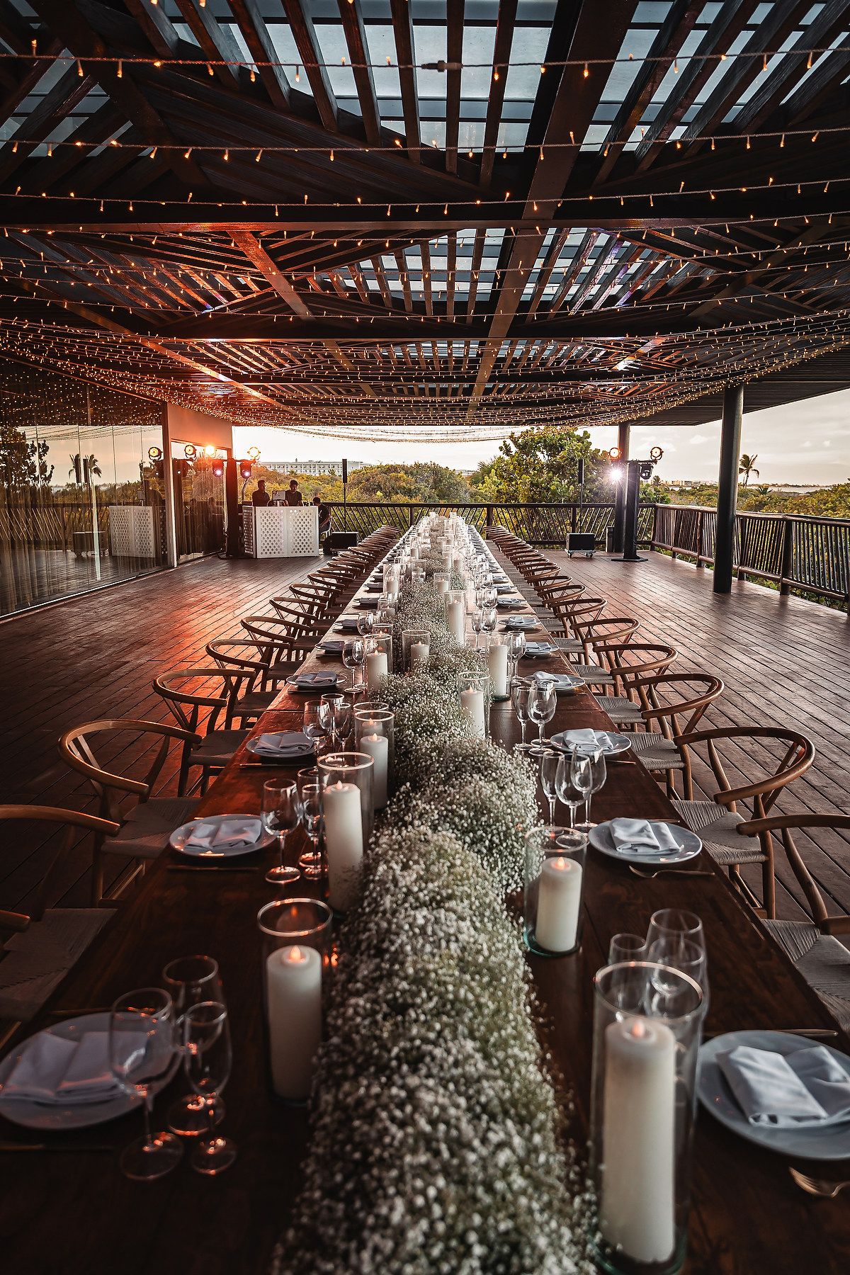 An elegant wedding reception table setup with baby's breath centerpieces and candles under wooden pergola.